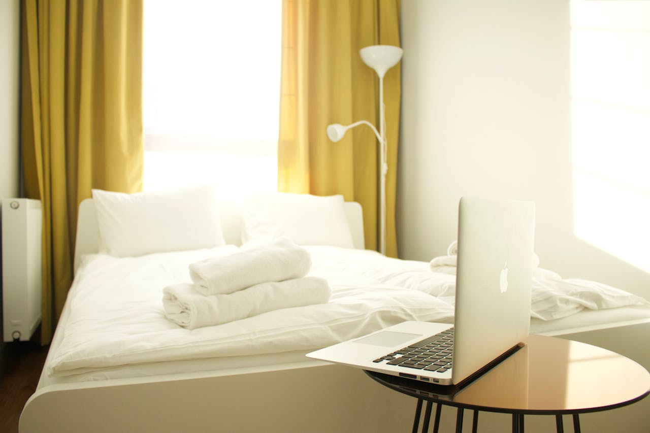 A serene modern bedroom featuring a laptop on a table, natural light, and comfortable design.